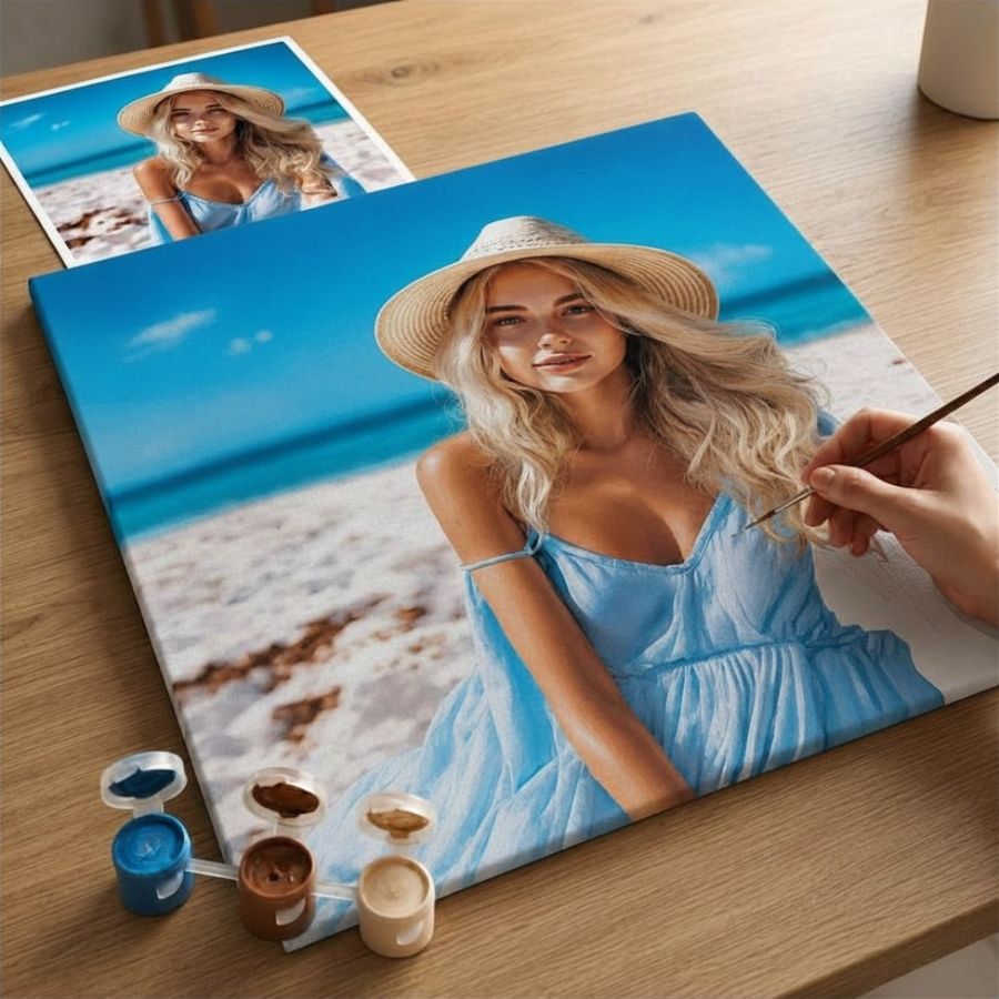 A custom canvas print of a woman painting on a beach, shown on a wooden table with paint pots and a paintbrush, alongside a reference photo of the portrait.