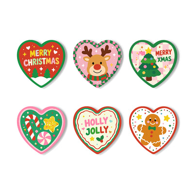 Six heart-shaped Christmas stickers arranged in two rows on a white background. The designs include a red 'Merry Christmas' tree, a pink reindeer with a green striped scarf, a green Christmas tree with 'Merry Xmas' text, candy canes and peppermint candies, a gingerbread man, and a 'Holly Jolly' heart. Christmas-Cheer Coasters - 6 Pack Paint by Numbers