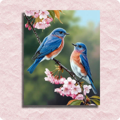 Two blue birds perched on a branch with pink flowers against a blurred green background. Eastern Bluebirds - Paint by numbers