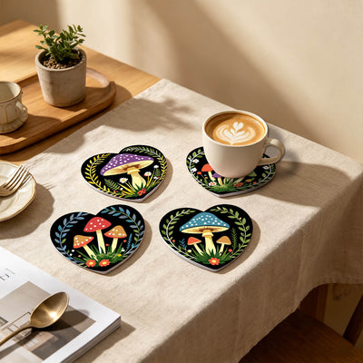 Four heart-shaped coasters with colorful mushroom and leaf illustrations arranged on a beige tablecloth, with a cup of latte on one coaster in a warm indoor setting. Enchanted Mushrooms Coasters - 6 Pack Paint by Numbers Lifestyle