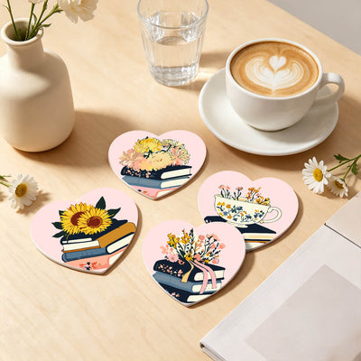 Four heart-shaped coasters with floral and book illustrations arranged on a light wood table next to a cup of latte, a small vase, and daisies. Floral Blossoms Coasters - 6 Pack Paint by Numbers Lifestyle