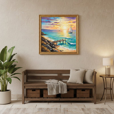 A framed square canvas painting of a colorful sunset seascape with sailboats, hung on a textured beige wall above a wooden bench in a styled living room. Mini Coastal Pier - Paint by numbers lifestyle