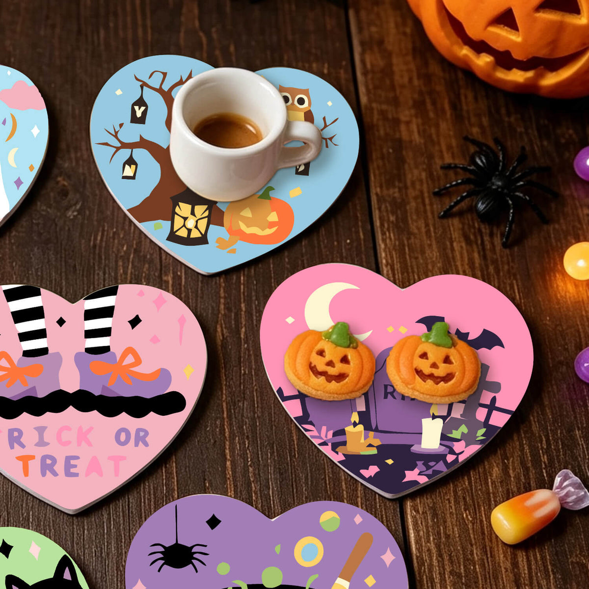 A set of heart-shaped wooden coasters with colorful Halloween designs, shown on a dark wooden table with cookies, a cup of coffee, candy corn, and a plastic spider decoration. Spooky Hearts - Coasters Paint by numbers Lifestyle
